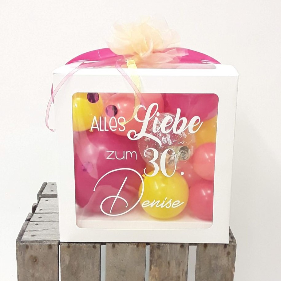 Ballonbox mit Aufdruck 'Alles Liebe zum 30. Denise', gefüllt mit pinken und gelben Ballons, verziert mit Schleife