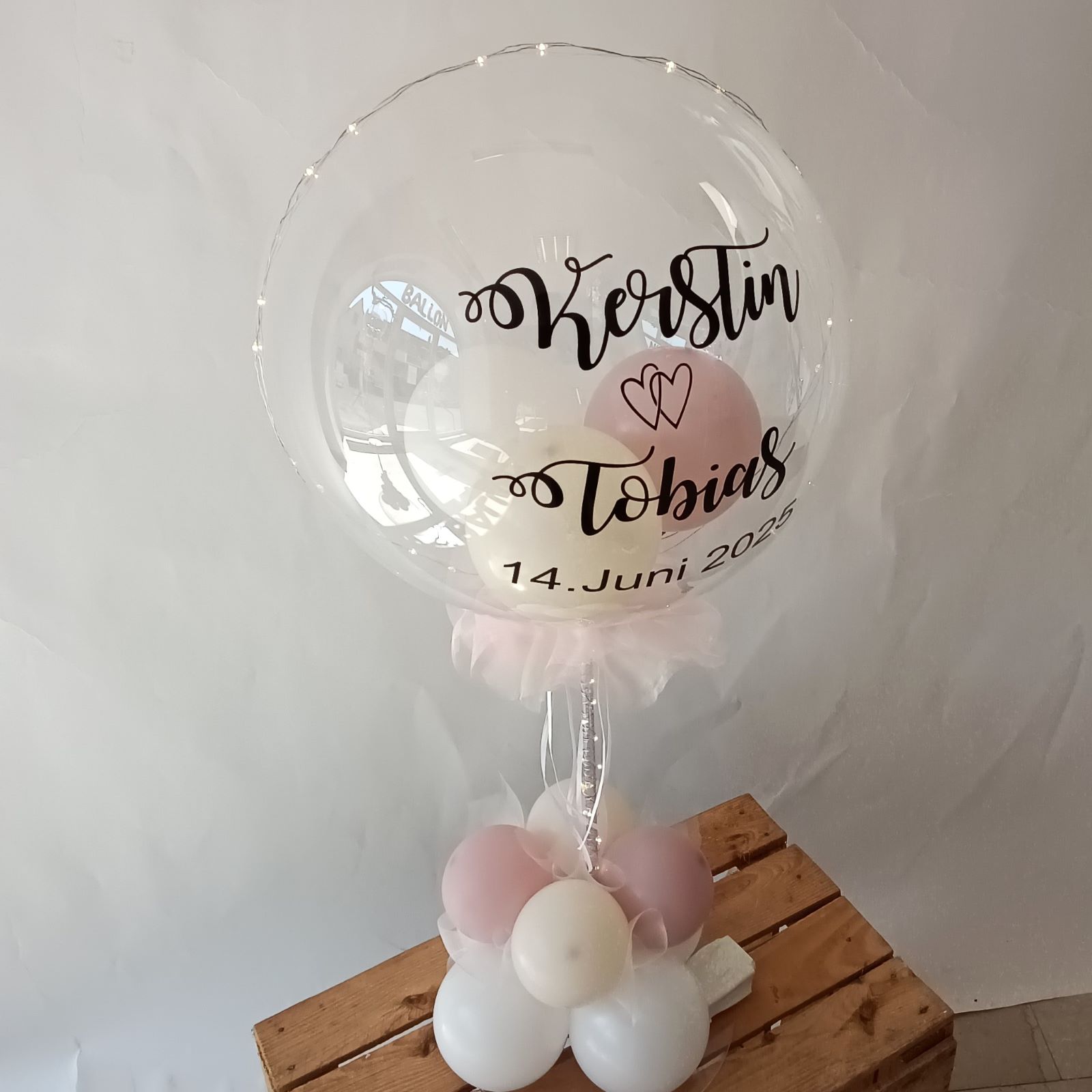 Transparenter Ballon auf Tischständer mit Namen 'Kerstin & Tobias' und Hochzeitsdatum, rosa-weiße Ballons.