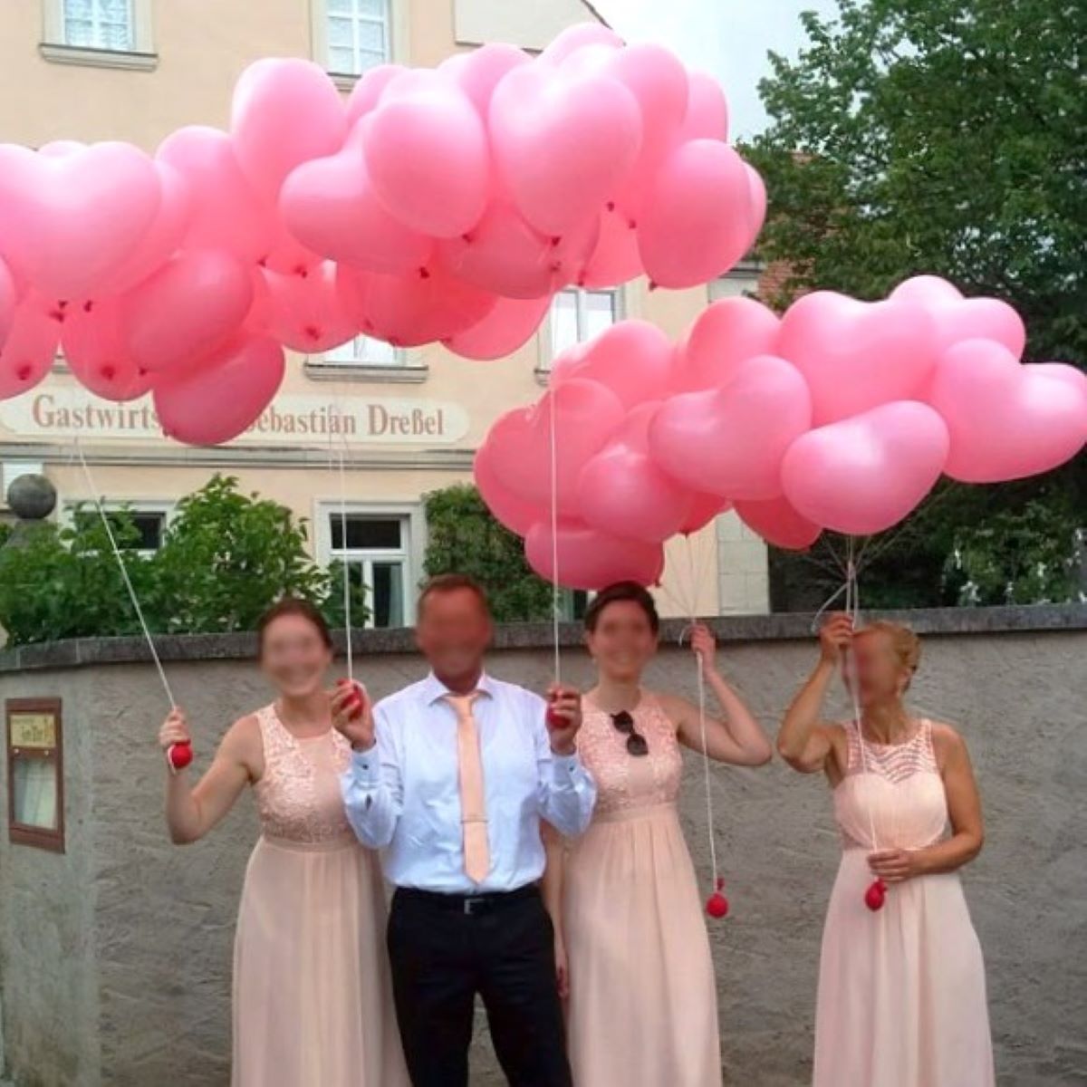 Vier Personen halten viele rosa herzförmige Heliumballons, bereit zum Steigenlassen