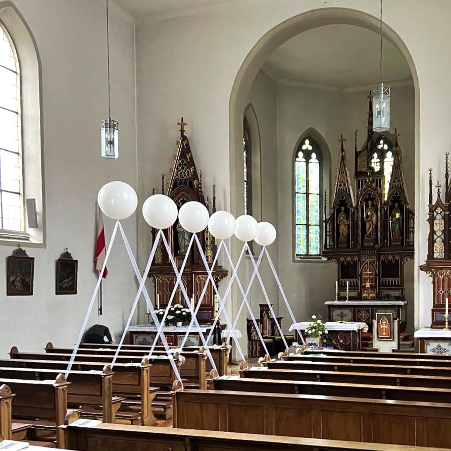 Reihe schwebender weißer Heliumballons mit Bändern, die beidseitig des roten Teppichs in einer Kirche angeordnet sind.-2