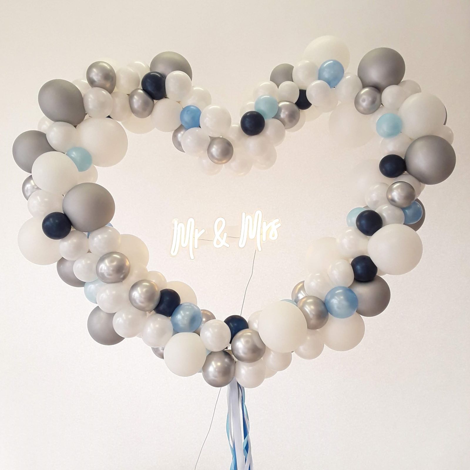 Herzförmiger Ballonbogen in vielen Farben mit unterschiedlich großen Ballons dekoriert und „Mr & Mrs“-Schriftzug in der Mitte blau
