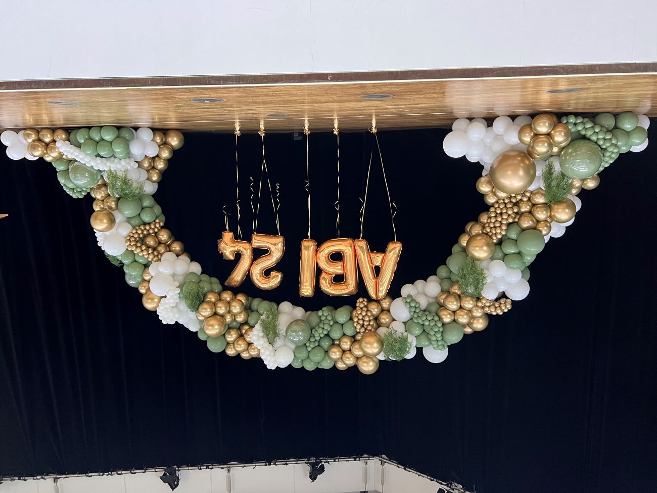 Große Ballongirlande auf Bühne in den Farben Grün, Weiß und Gold mit goldenem Schriftzug 'ABI 24' aus Folienballons, dekoriert mit Farn1