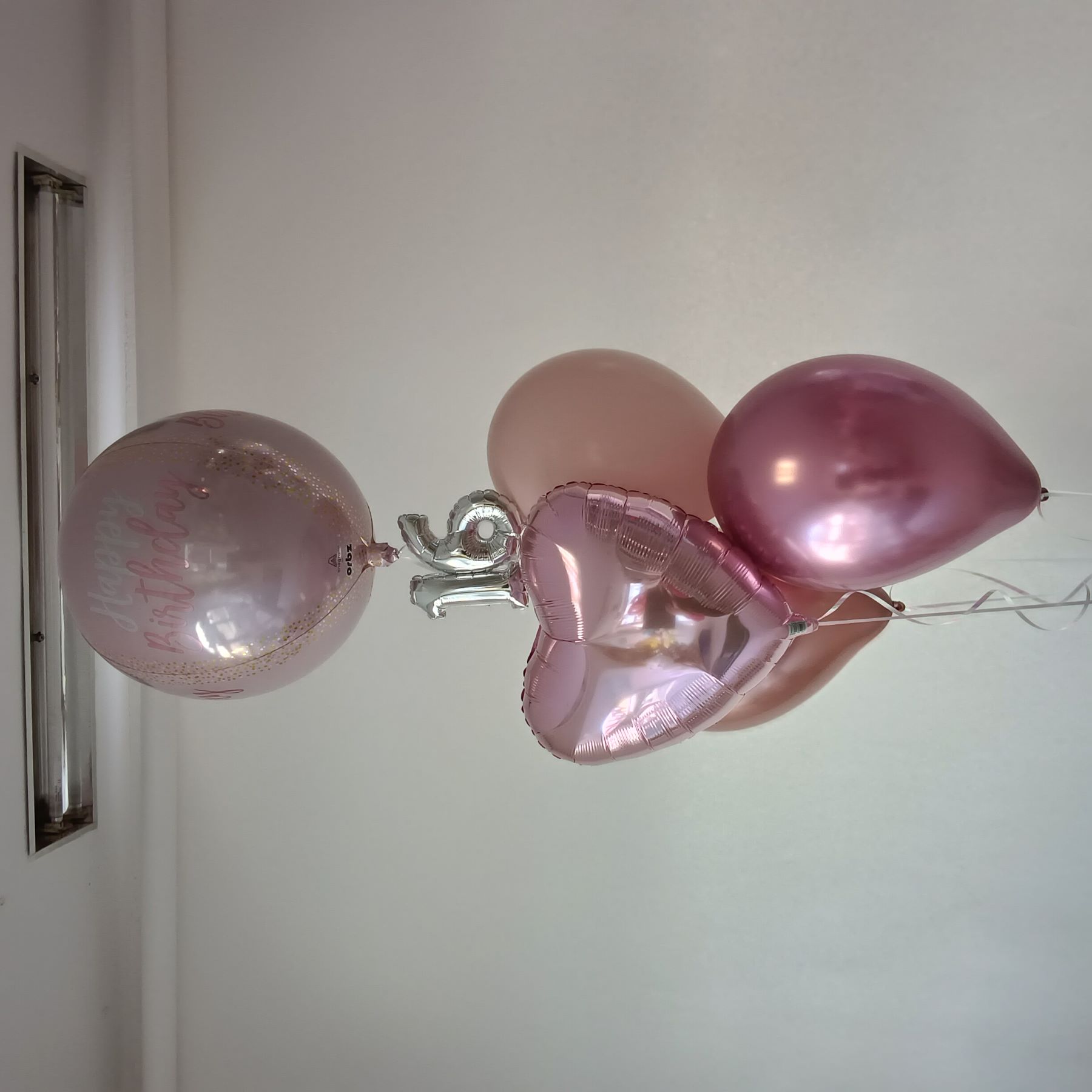 Ballonbouquet in Rosa- und Rosétönen mit einem herzförmigen Folienballon, Latexballons und silbernen Zahlenballons 1 und 6 darunter, sowie einem bedruckten Ballon mit 'Happy Birthday'.