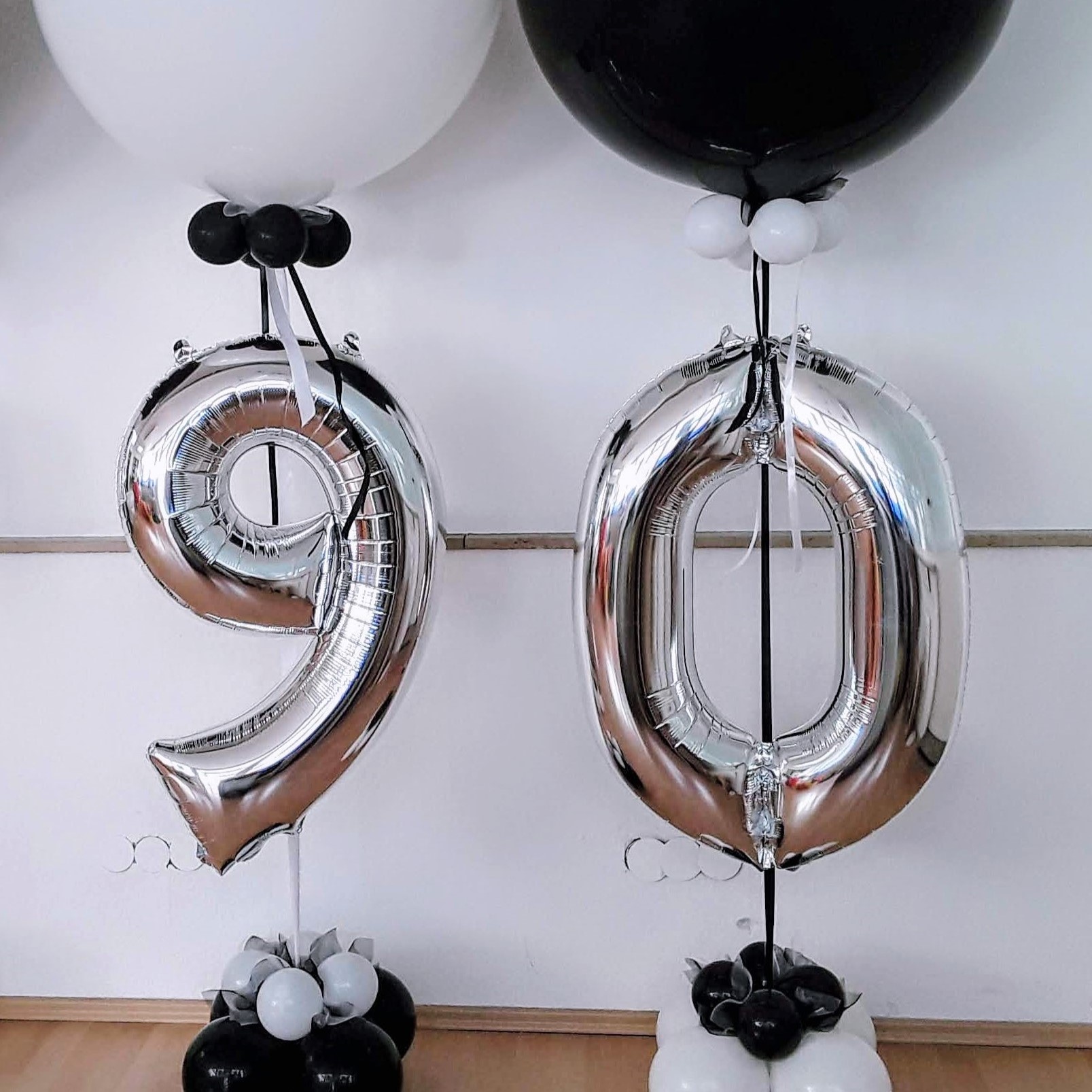 Große Zahlenballons 9 und 0 in Schwarz, Weiß und Silber, auf einem stabilen Ständer arrangiert zum Geburtstag