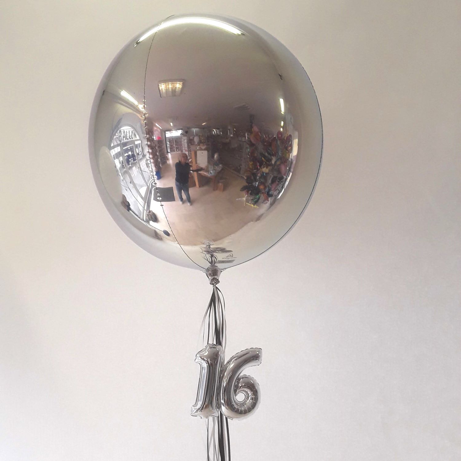 Silberne Ballonkugel mit schwebenden silbernen Zahlenballons 1 und 6 darunter.